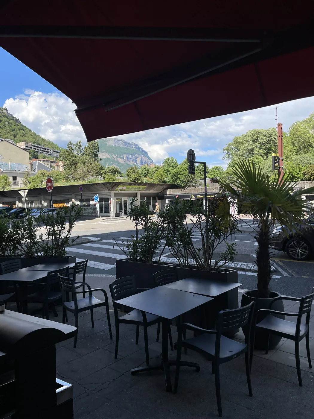 Terrasse du restaurant turc Cappadoce, rue de Belgrade à Grenoble — tables en terrasse, store rouge, palmiers et massif de la Chartreuse en arrière-plan
